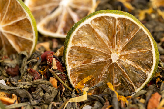 bright large dry lime slices and green tea with pieces of fruit, natural green tea with added flavors and pieces of fruit and cut dried limes, close up