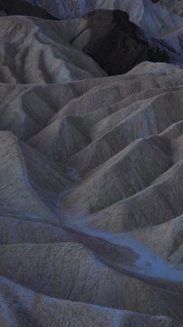 Vertical Screen: Eroded mudstone badlands at Zabriskie Point in Death Valley National Park California during blue hour twilight with dramatic ridges and sedimentary rock formations creating waves.
