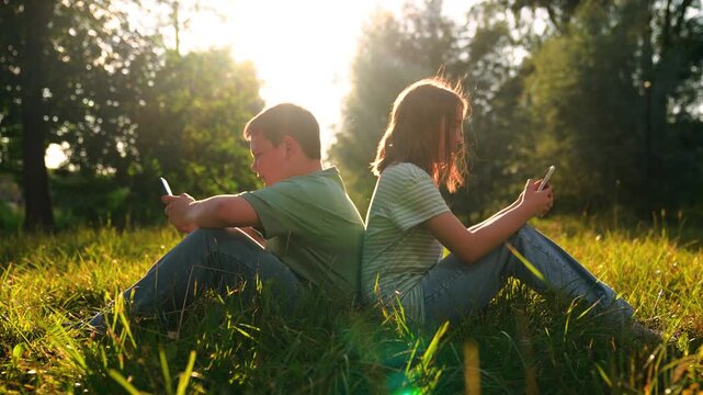 Teens on mobile phones outside, Sunset glow across meadow, Digital natives relaxing in nature, Friends connected by screens, Park day smartphone snapshot, Golden hour lifestyle image, Green field tech
