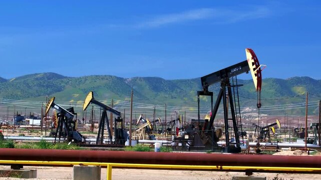 Oil Pump Jacks Pumping Crude Oil in Desert Landscape Against Blue Sky