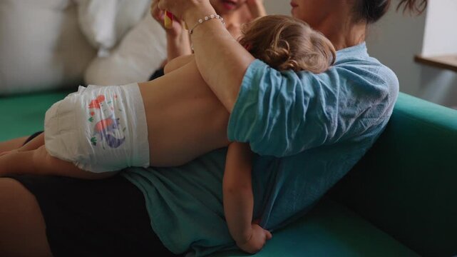 Toddler resting across mother&rsquo;s lap on sofa during quiet family moment capturing comfort, attachment and authentic everyday parenting connection
