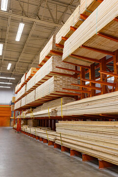 Large bundles of structural wooden lumber and timber planks stacked neatly on high heavy-duty orange cantilever storage racks inside a spacious home improvement warehouse or building supply center, US
