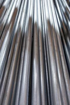 Close-up low-angle perspective view of shiny metallic rigid galvanized steel conduits and shiny metal electrical pipes stacked tightly together inside a building materials warehouse, USA
