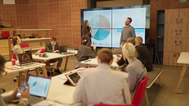 Business colleagues engage in a dynamic presentation with data analytics on a large screen. Employees attentively participate in a corporate meeting held in a contemporary office environment.