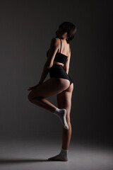 Fototapeta premium Model poses in black attire with white socks against a dark background