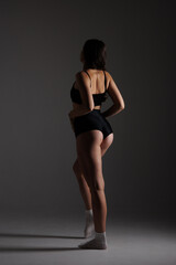 Fototapeta premium Model poses in black clothing highlighting body silhouette against a dark background