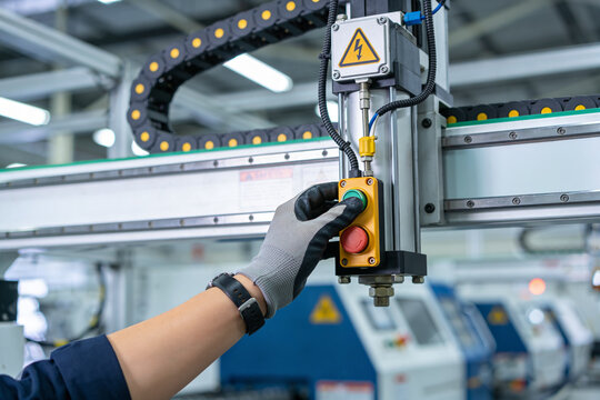 Worker's gloved hand presses green button on industrial automation machinery