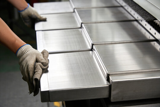 Worker's hands in protective gloves carefully handling polished metal sheets on a factory line