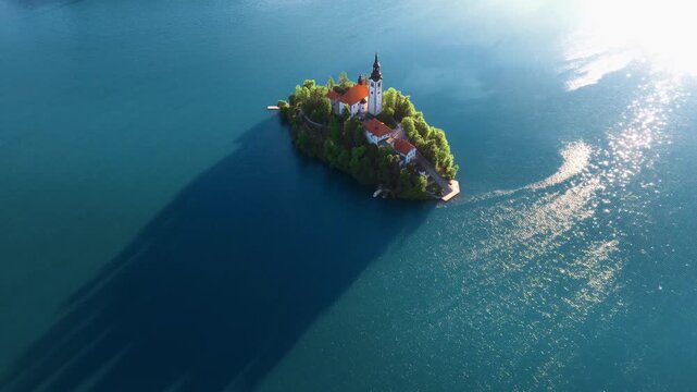 Aerial view of Bled Island featuring the Church of the Assumption surrounded by the turquoise waters of Lake Bled with sunlight reflections Bled, Radovljica, Slovenia.