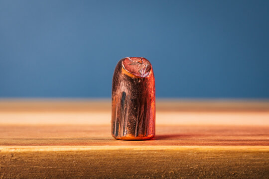 Fired and deformed 357 caliber copper bullet standing on a wooden surface against a blue background, close up of damaged rifle projectile