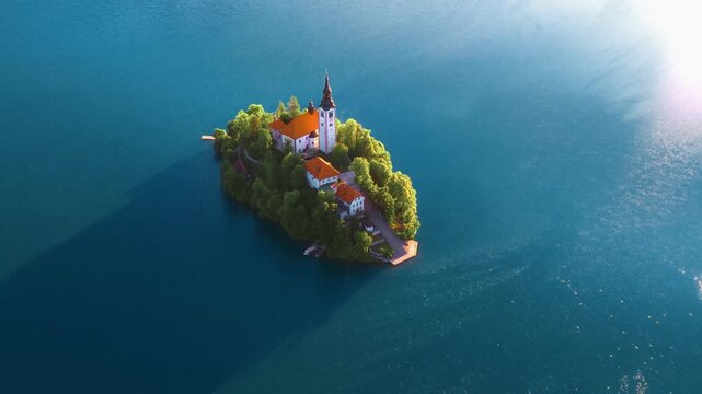 Aerial view of the Church of the Assumption on Lake Bled Island surrounded by calm blue waters and lush green trees in Bled, Radovljica, Slovenia.