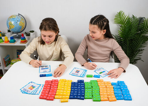 Elementary students using domino tiles and flashcards to build words and practice spelling. Creative language arts lesson for children isolated on a white studio background.