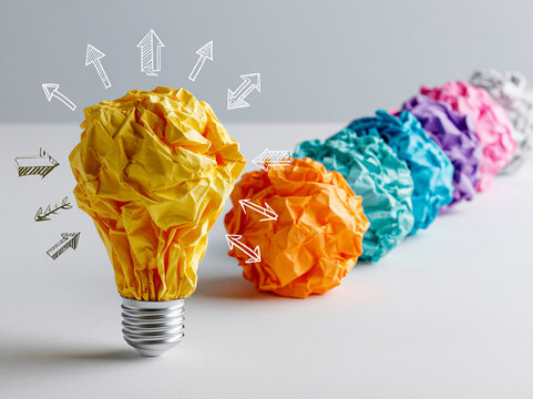Colorful crumpled paper balls arranged in a line with a light bulb shape in a bright setting in a creative workspace