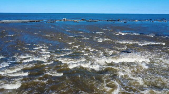 Aerial view of powerful spring runoff pouring from Rivi&egrave;re Blanche toward rocky reefs and erratic boulders along the St. Lawrence coastline in Gasp&eacute;sie.
