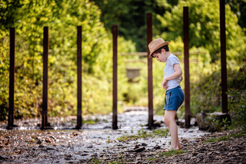 Thoughtful boy standing barefoot by shallow forest river looking down © Oleksii Yemelianov