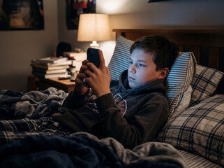 Fototapeta premium Young boy using mobile phone in bed late at night in dark room