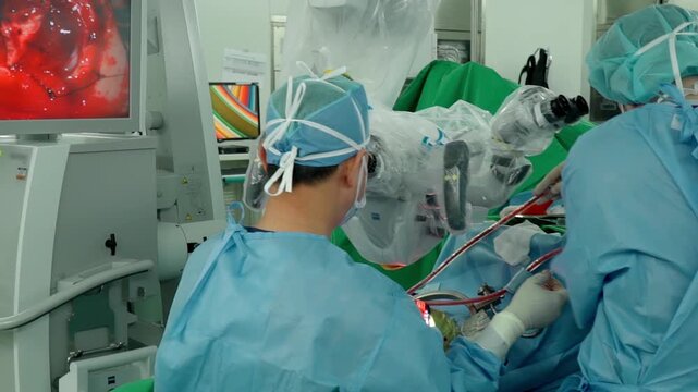 A medical professional performs a delicate brain neurosurgery procedure using an operating microscope in a surgical room surrounded by advanced monitoring