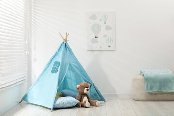 Wigwam, toy bear, pouf and pillows near white wall in child's room © New Africa