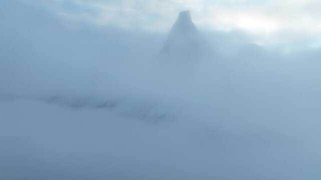 Aerial view of the sharp Stetind mountain peak emerging from a sea of thick white clouds and fog in Narvik Municipality, Nordland, Norway.
