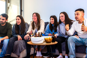 Obraz premium Diverse friends watching sports on tv at home, cheering for their team with snacks and beer