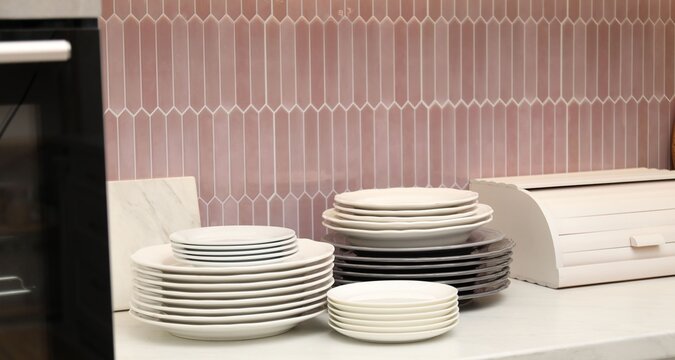 Set of clean plates and breadbox on white countertop in kitchen