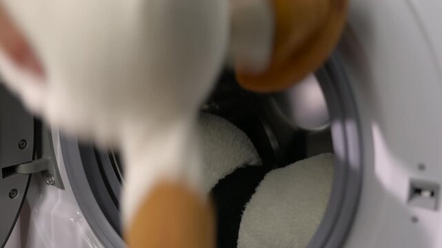 Woman putting stuffed animals in washing machine for cleaning. Close-up of a female hand loading plush toys, including a teddy bear, into the drum of a modern washing machine for a gentle wash cycle