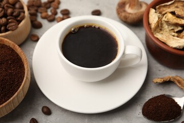 Obraz premium Cup of coffee, beans, powder and mushrooms on light grey table, closeup