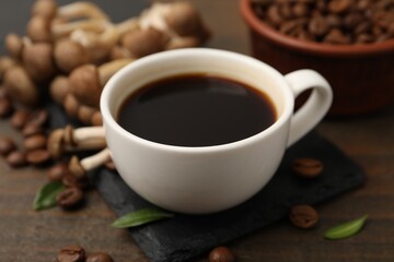 Obraz premium Cup of coffee, beans and mushrooms on wooden table, closeup
