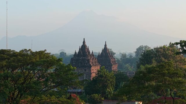 Aerial view of the twin stone structures of Plaosan Lor Temple surrounded by lush green trees with Mount Merapi in the background Kecamatan Prambanan, Jawa Tengah, Indonesia.