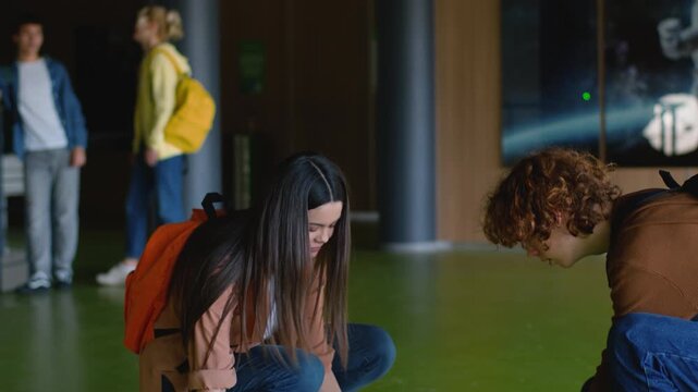 Caucasian student girl fall books on floor in school boy help pick up friends woman female schoolgirl drop textbooks copybooks clumsy guy male teenager friendship support love teen education helping