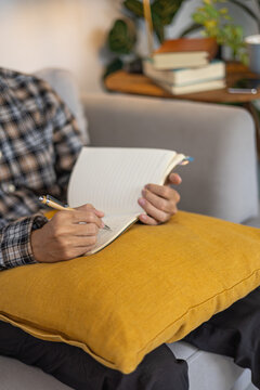 Creative writer taking notes, journal or brainstorming in a book indoors sitting on sofa at home.