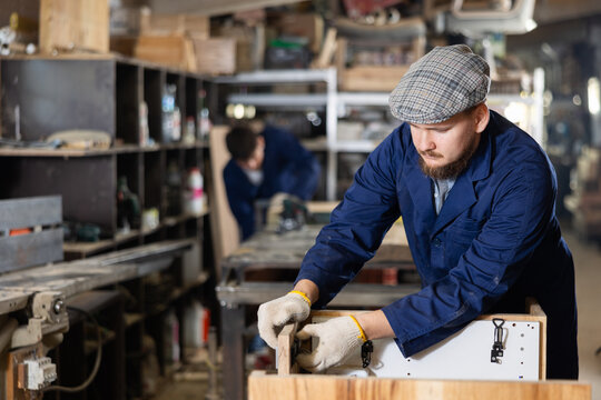 Experienced furniture assembler assembles wooden table at furniture factory