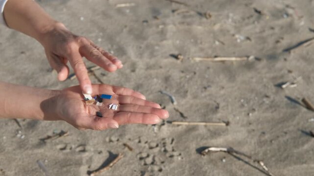 Person collecting microplastics on a polluted beach. Volunteer's hands collecting and showing small pieces of microplastic waste from the sand, demonstrating the problem of environmental pollution