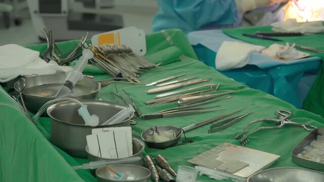 Surgical clamps and medical equipment on green surgical tray inside operating room.