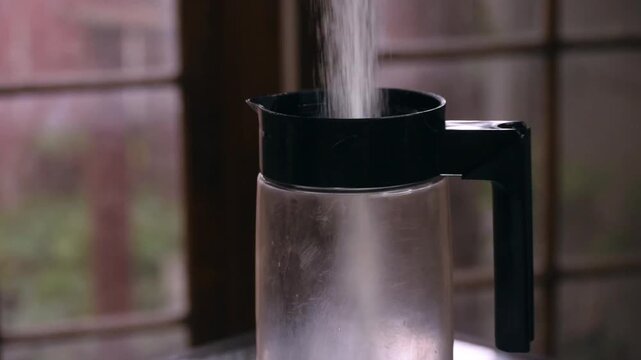 Flowing sugar pouring smoothly into a clear plastic jar during morning tea making ritual. Done in the soft glow of the lights inside the kitchen