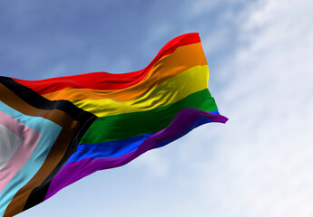 Naklejka na ściany i meble Progress Pride Flag ripples in the wind against a blue sky with soft clouds. 3D rendered illustration of the inclusive LGBTQ+ symbol for diversity and equality.