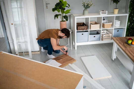 Man assembling furniture with electric drill at home