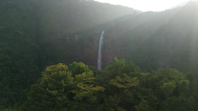 Aerial view of Cikanteh Waterfall cascading down a cliff surrounded by lush tropical forest and morning mist in Sukabumi, West Java, Indonesia.