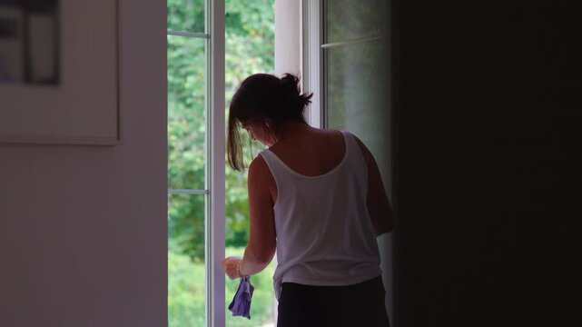 Woman wiping window glass while letting fresh air into home concept of ventilation cleanliness and everyday routine