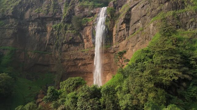 Aerial view of Cikanteh Waterfall cascading down a massive rocky cliff surrounded by lush tropical forest and green vegetation in Sukabumi, West Java, Indonesia.