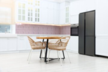Fototapeta premium Blurred view of stylish kitchen interior with wooden table and chairs