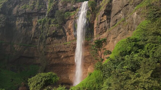 Aerial view of Cikanteh Waterfall cascading down a steep rocky cliff surrounded by lush green tropical vegetation in Sukabumi, West Java, Indonesia.