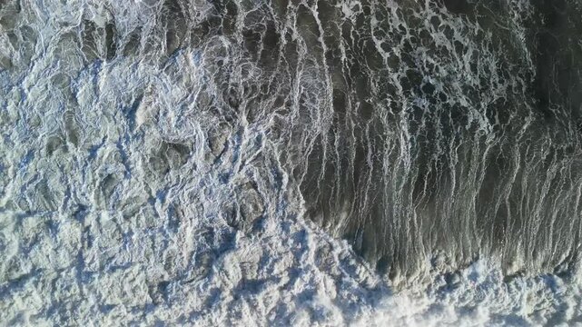 Aerial view of crashing waves and white sea foam at Ujung Genteng Beach in Kecamatan Ciracap, Jawa Barat, Indonesia.
