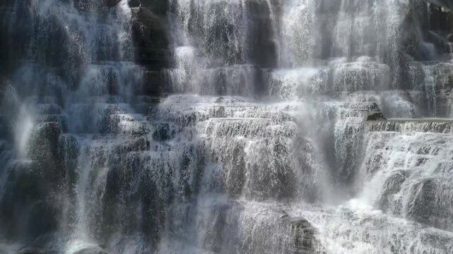 Aerial view of Cigangsa Waterfall with water cascading over tiered dark rock formations and rising mist in Sukabumi, West Java, Indonesia.