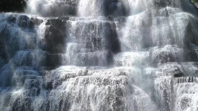 Aerial view of Cigangsa Waterfall with multi-tiered cascades of white water flowing over dark stone walls in Sukabumi, West Java, Indonesia.