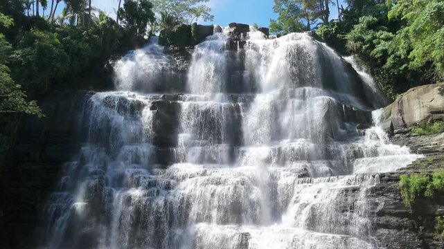Aerial view of Cigangsa Waterfall with cascading white water over tiered rock formations surrounded by lush tropical greenery, Sukabumi, West Java, Indonesia.