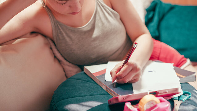 Deeply focused and worried high school girl making secret notes and tiny cheat sheets from her mobile phone, preparing for a test while sitting on a couch under warm indoor lighting.