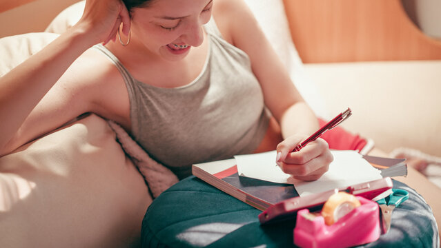 Deeply focused and worried high school girl making secret notes and tiny cheat sheets from her mobile phone, preparing for a test while sitting on a couch under warm indoor lighting.