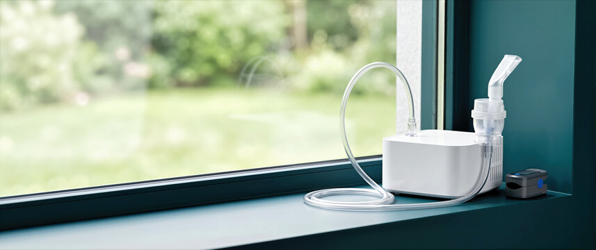 White nebulizer machine and pulse oximeter on a teal window ledge. Respiratory care and health monitoring equipment at home. Copy space for text