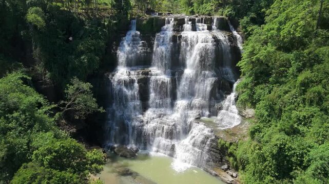 Aerial view of Cigangsa Waterfall cascading over tiered rock formations surrounded by lush tropical forest in Sukabumi, West Java, Indonesia.